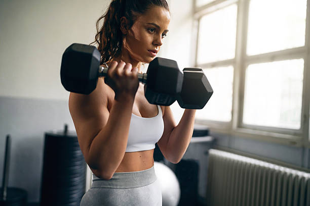 istock Focused young woman lifting dumbbells during a workout in a bright gym 2210688057