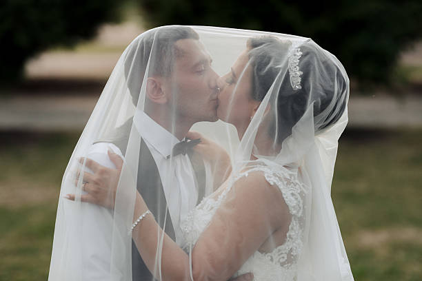 Cropped shot of an affectionate young newlywed couple smiling at each other while covering themselves with a veil on their wedding day