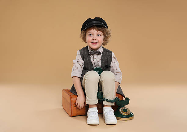 Cute little boy with old telephone and suitcase on beige background