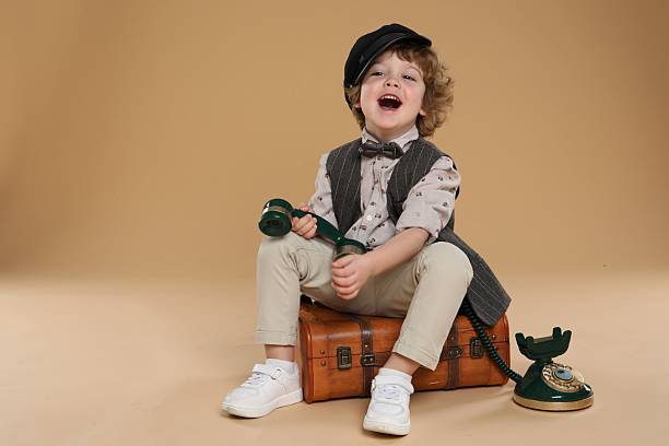 Cute little boy with old telephone and suitcase on beige background, space for text