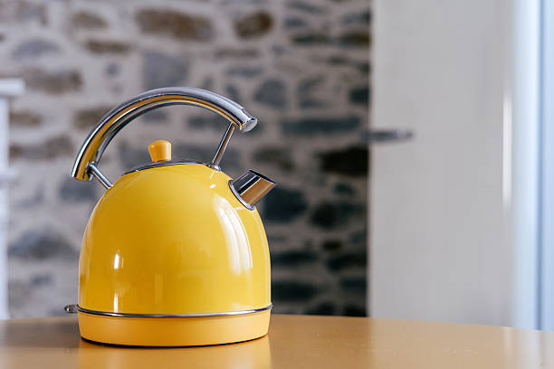 A vibrant yellow kettle sits on a wooden kitchen table, showcasing a blend of modern and classic design elements in a cozy home environment
