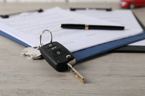 Car key and purchase agreement on wooden table, closeup. Buying auto