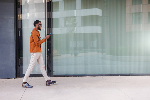 istock Man walking outdoors while using a mobile phone in front of the glass door 2210693183