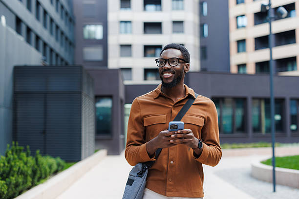 istock Smiling man outdoors holding a smartphone near modern buildings 2210693295