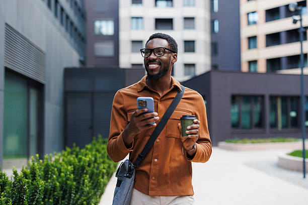 istock Smiling man walking outdoors holding a smartphone and a coffee cup 2210693442