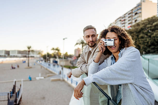 istock Young Couple Enjoying Scenic Moment by Beachside Promenade with Camera 2210694064