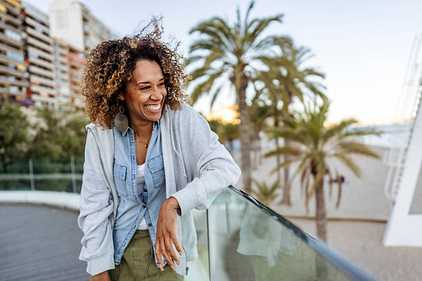 istock Smiling Woman Relaxing Outdoors by a Beachside Balcony with Palm Trees 2210694509