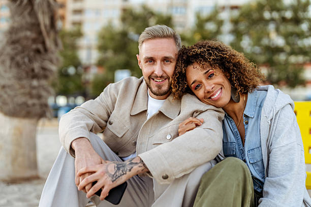 istock Happy Couple Sitting Outdoors Smiling at Camera on a Sunny Day 2210695218
