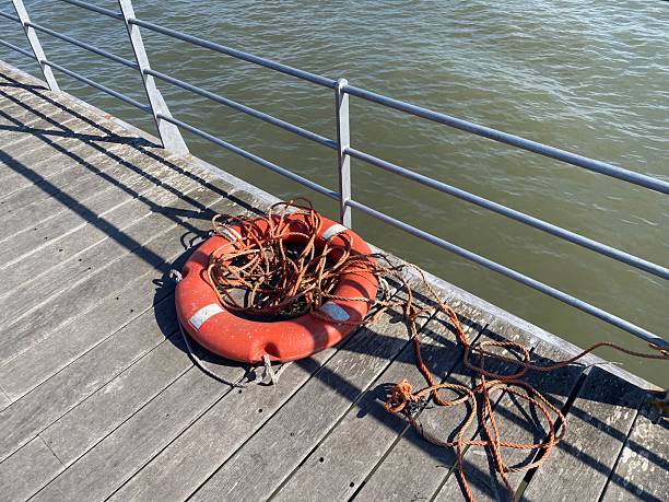Weathered lifebuoy with tangled rope on wooden pier. Sunlight and shadows create a raw, nautical atmosphere. Conceptual image of rescue, neglect, or passage of time.