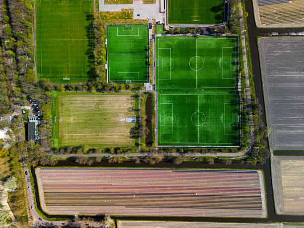 istock A top-down aerial view of multiple football fields surrounded by blooming tulip fields and narrow canals, blending sports infrastructure with the colorful Dutch agricultural landscape. 2210698805