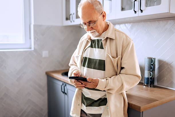 istock Senior man text messaging on mobile phone in the kitchen 2210705047