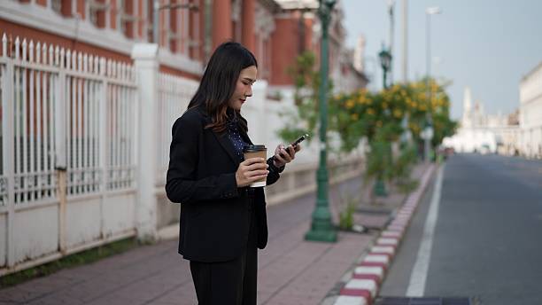 istock asian female using smartphone and holding coffee while standing on city sidewalk 2210706026