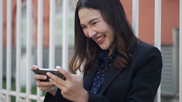 istock happy asian woman playing mobile game with joyful expression on smartphone closeup 2210706074