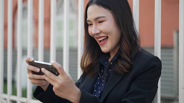 istock smiling asian woman playing smartphone game outdoors with happy expression 2210706082