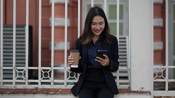 istock asian woman in black suit smiling and browsing smartphone while holding coffee cup 2210706091