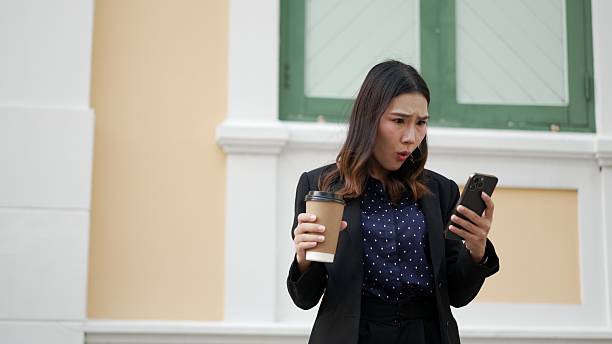 istock young asian woman reacting with shock while holding phone and coffee 2210706480
