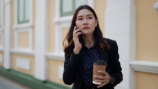 istock Asian woman talking on phone while holding coffee outside office building 2210706509