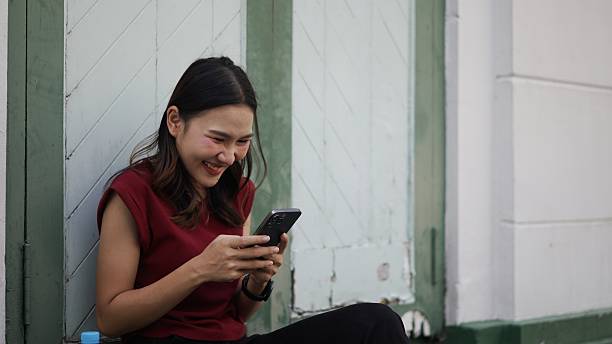 istock cheerful asian woman laughing while using smartphone outdoors, casual lifestyle and digital connection 2210706716
