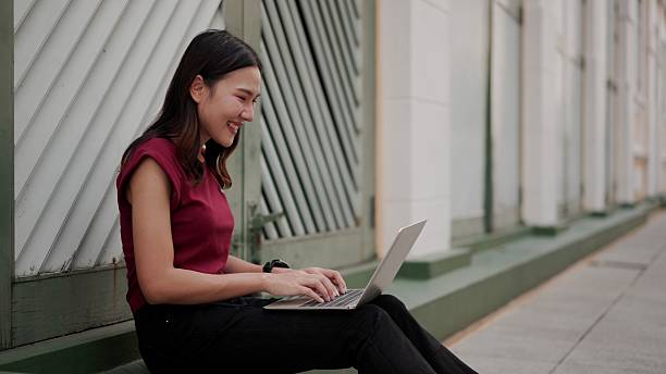 istock asian woman smiling while using laptop on city sidewalk, working remotely with happy and focused mood 2210706816