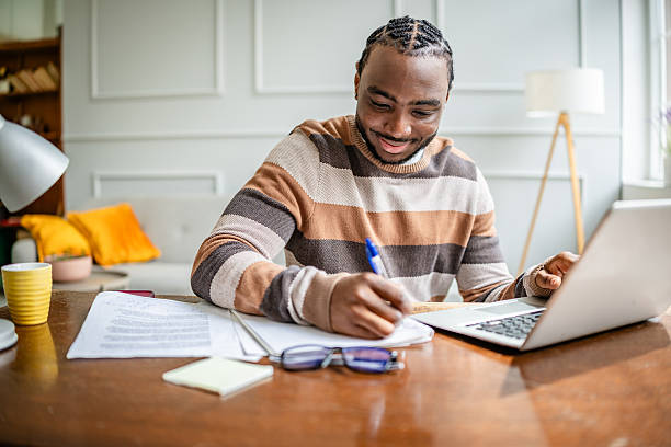 istock Young man engaged in online learning at home while smiling and taking notes during a virtual class session 2210716339