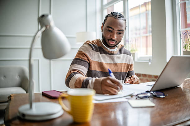 istock Young man engaged in online learning at home, focusing on his studies with a laptop and study materials 2210716888