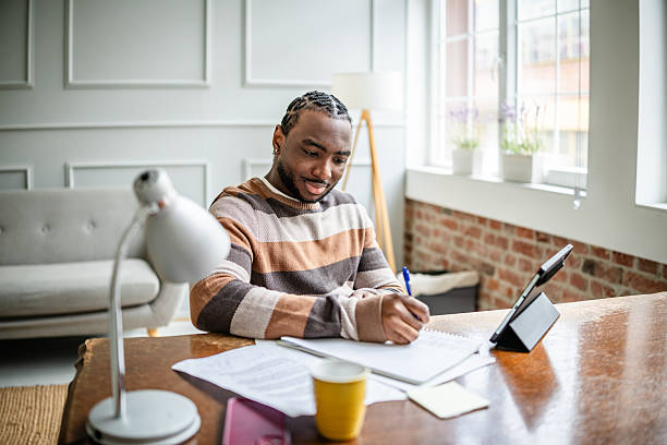 istock Young man engaged in online learning at home, happily studying and taking notes in a cozy living room environment 2210716993