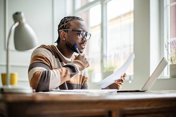 istock Young man engaged in online learning at home, studying with laptop and notes in bright living room 2210717042