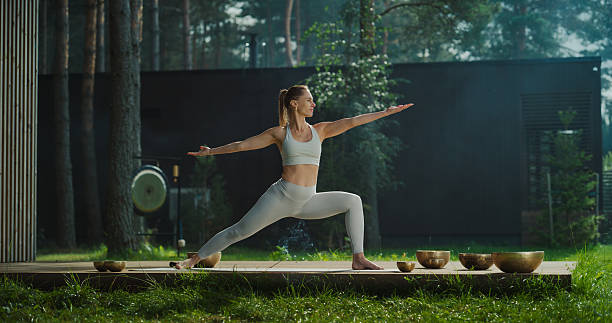 istock Serene Caucasian Female Practices Yoga in a Tranquil Forest Setting, Gracefully Transitioning Through Poses on Wooden Platform with an Incense Stick, Surrounded by Nature and Singing Bowls 2210735715