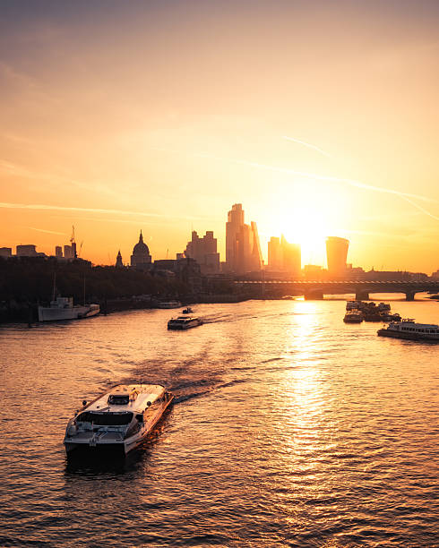 London, England, United Kingdom - 11th April 2025: An Uber boat passes along the River Thames at sunrise with St Paul's Cathedral and the silhouetted skyscrapers of the City of London in the distance