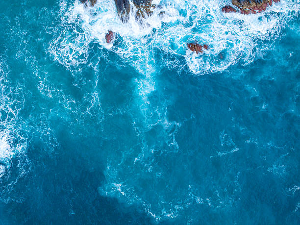 Vivid ocean water flows over rocks, creating foam and splashes in a dynamic display of nature's beauty under bright sunlight.