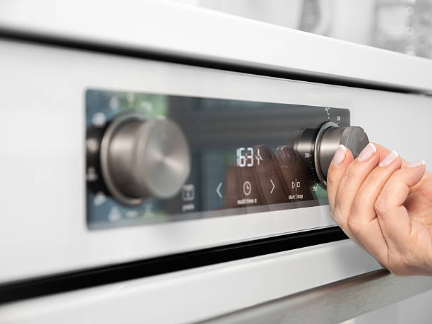 istock Woman adjusting modern white oven in kitchen.  Female hand pushing and turning knobs on oven control panel 2210744762