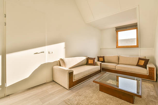 Fragment of a room with a sofa and table, a window with tulle. Living room with large sofa, pillows, coffee table, laminate flooring.
