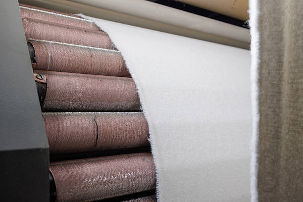 istock White fabric being processed through spinning rollers in an industrial textile manufacturing line. 2210754439