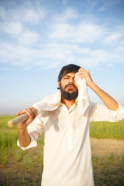 istock A hardworking Pakistani Indian farmer wipes sweat from his face while carrying a hoe, standing in a sunlit agricultural field. 2210757272