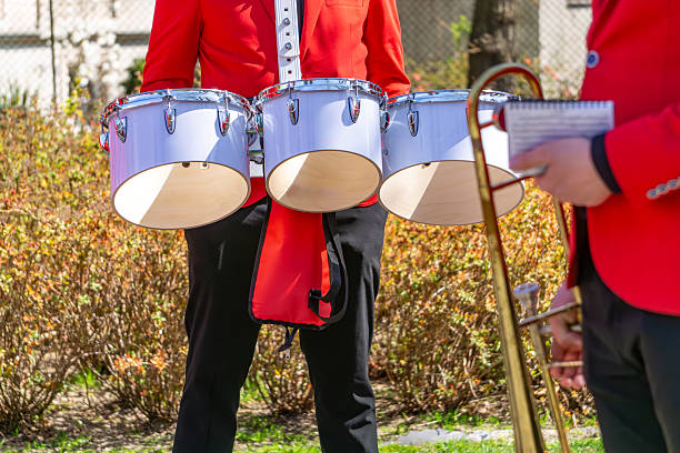 istock Musicians in red uniforms playing wind and percussion instruments during an outdoor performance. In the foreground are snare drums worn on harnesses. 2210762361