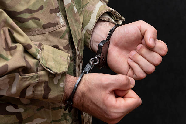 istock A soldier in a military camouflage uniform is handcuffed on a black background. 2210770344
