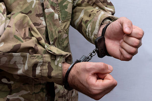 istock A soldier in a military camouflage uniform is handcuffed on a light background. Concept: a military tribunal over a criminal, an army court. 2210770350