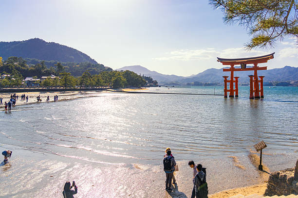 Miyajima, Japan - People near the water's edge around the Itsukushima Shrine Torii Gate.