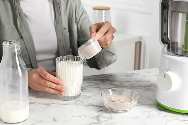 istock Making protein cocktail. Woman adding powder into glass with milk at white marble table, closeup 2210778251