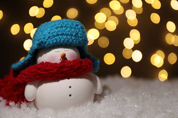 istock Cute decorative snowman on artificial snow against blurred lights, closeup. Space for text 2210778706