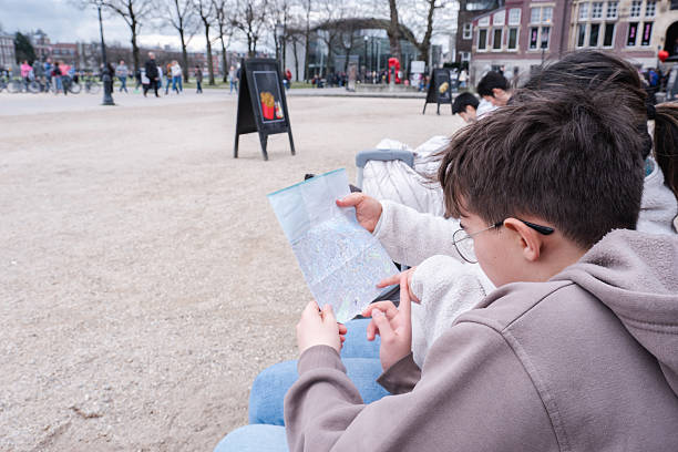 A tourist woman and her son sit on a bench in Amsterdam, luggage by their side, exploring a city map together. A candid travel moment at the start of their adventure.