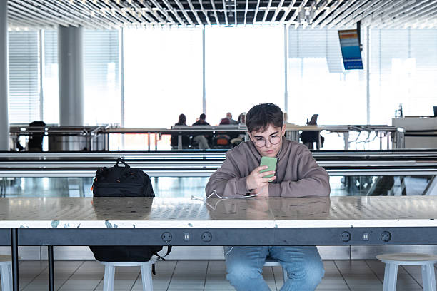 A young male traveler waits at the airport, passing time before his flight. A relaxed travel moment capturing the start of a new journey.