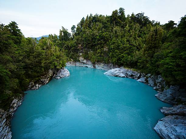 Turquoise blue glacial river water winding through white granite rock cliffs canyon with lush green tree forest at Hokitika Gorge Kokatahi West Coast South Island New Zealand