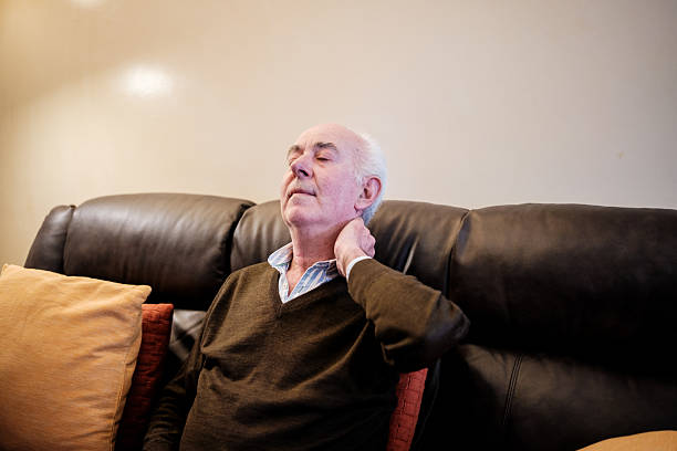 istock Senior man suffering from neck pain while sitting on sofa 2210786130
