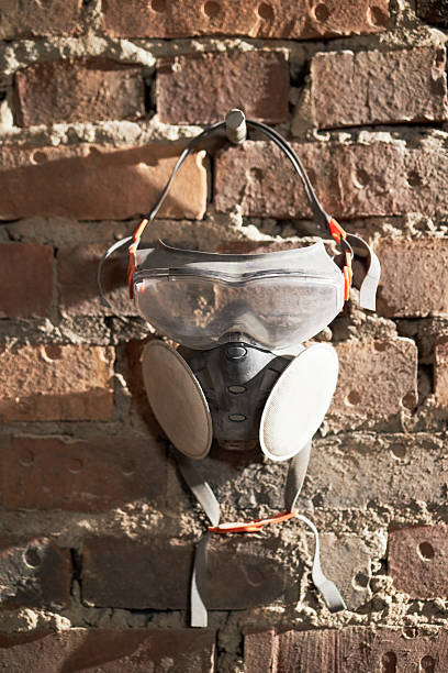Vertical shot of dirty respirator hanging on nail with brick wall in background