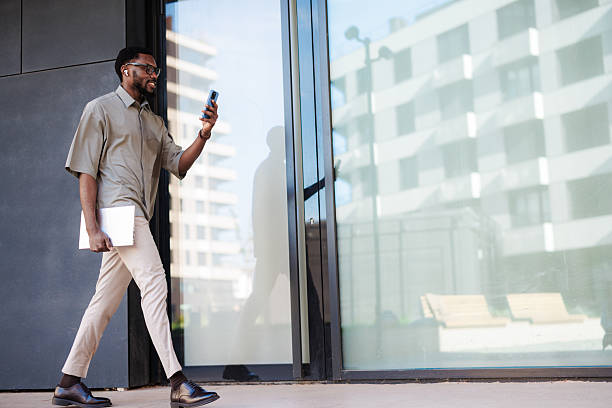 istock African American man walking outside while using smartphone and holding laptop 2210787214