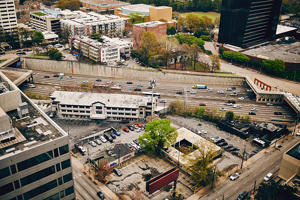 Aerial view of a bustling urban cityscape featuring a busy highway, modern buildings, residential structures, and scattered greenery on a cloudy day.