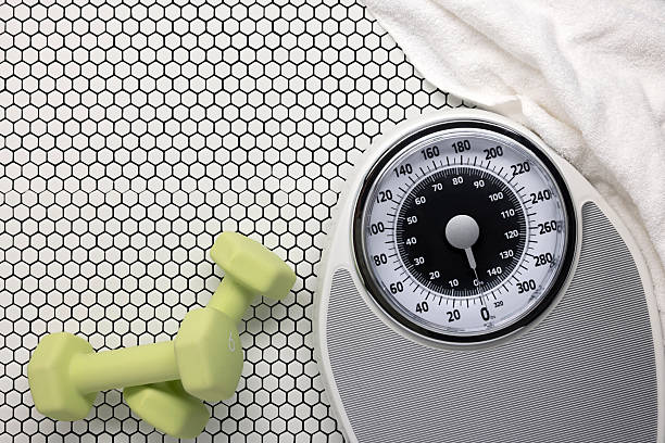 istock Bathroom scale and bath towel on retro white tile floor and exercise weights 2210795471
