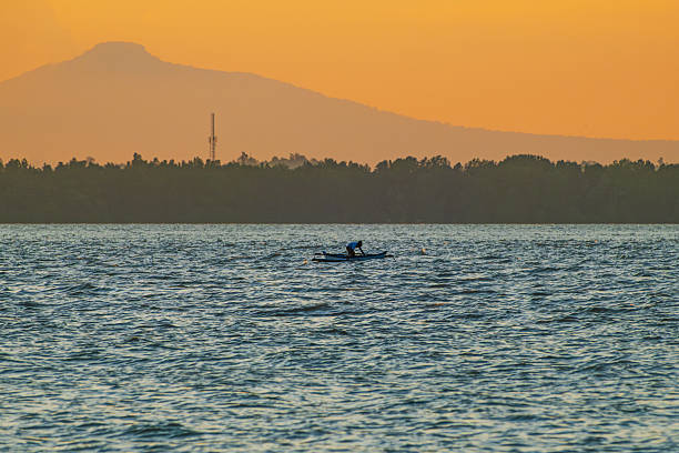The fisherman is pulling his net in Balikpapan Bay, with mountain in the background.