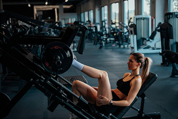 Woman focusing on her workout, adding a weight plate to a leg press machine at the gym, building strength